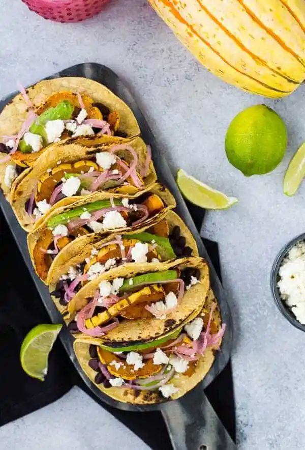 Overhead of tacos, with squash, limes, and cheese nearby.