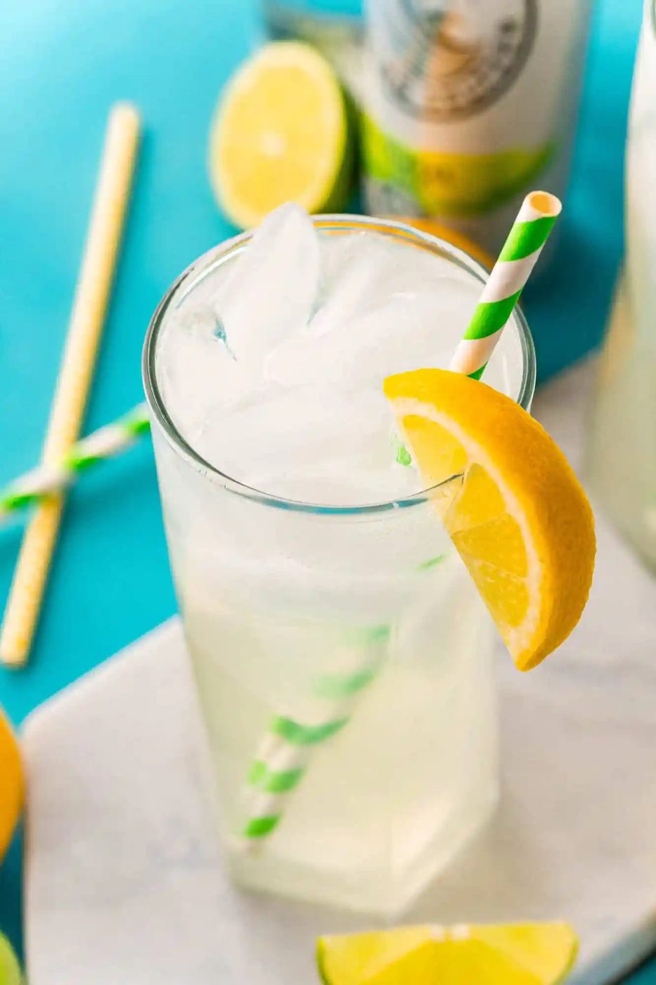Glasses of iced beverage with a green and white paper straw and an orange wedge.