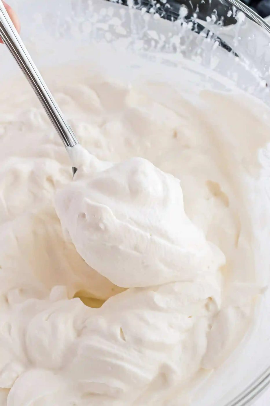 Freshly whipped cream, on a spoon, in a mixing bowl.