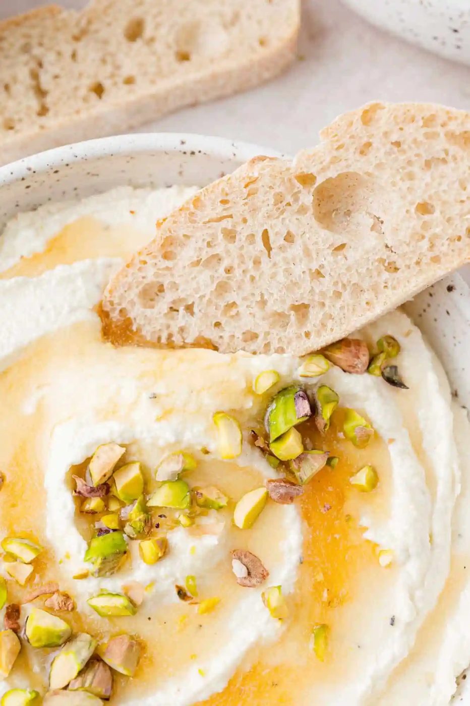 Bread being dipped in whipped feta topped with honey and pistachio.