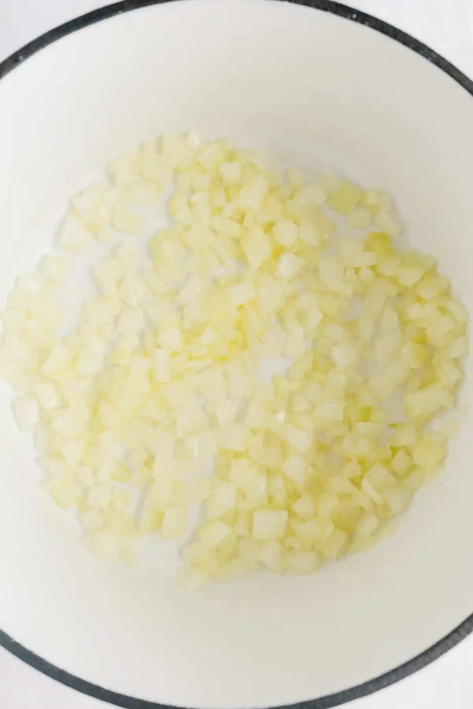 Diced onions cooking in a white pot.