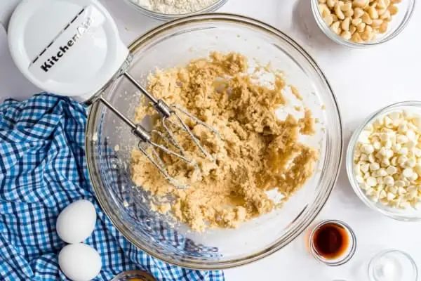 Cookie dough ingredients beaten together in a mixing bowl next to a hand mixer.