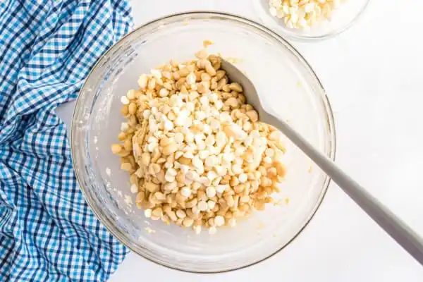 Macadamia nuts and white chocolate chips added to a mixing bowl of cookie dough.
