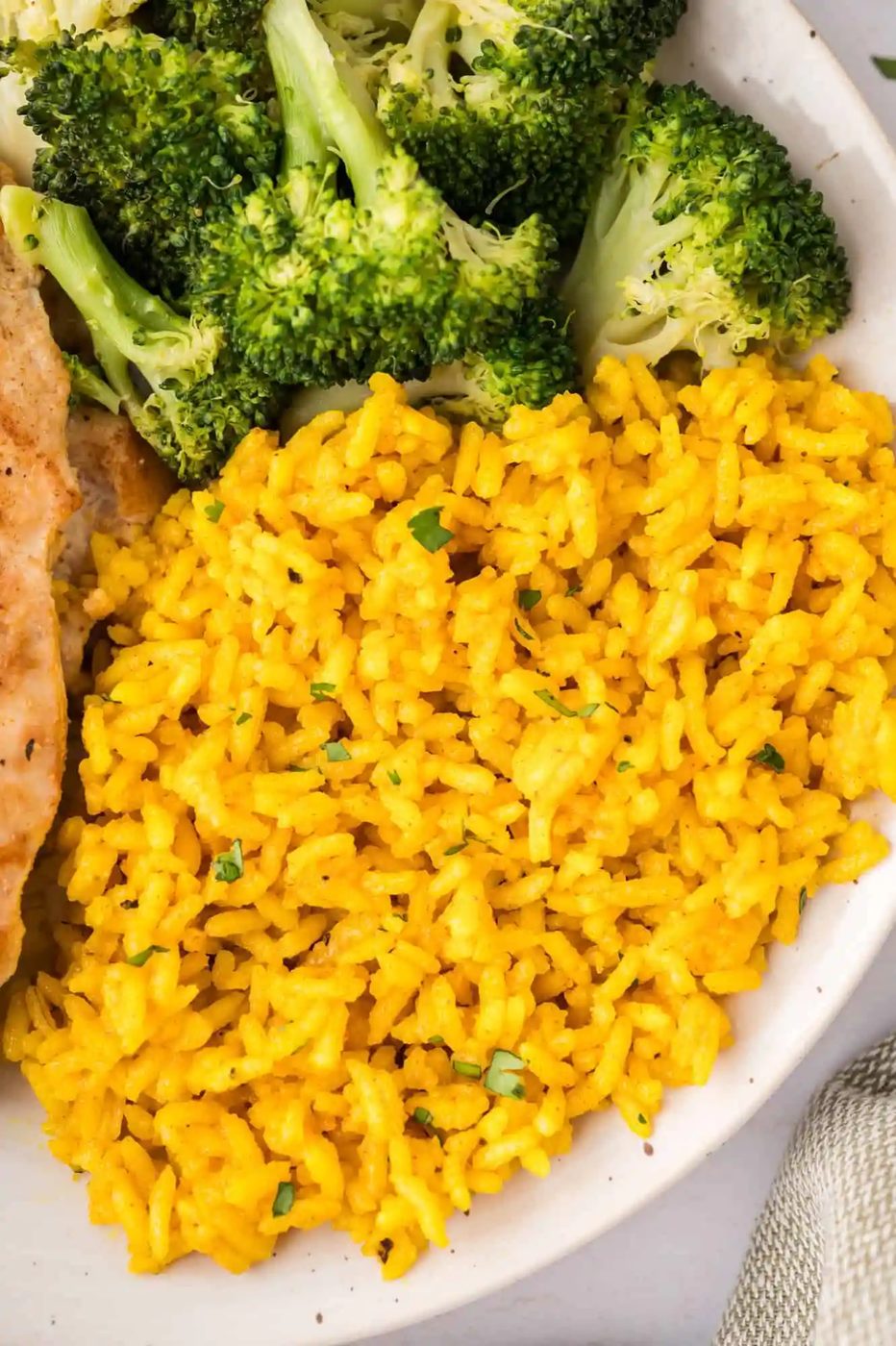 A plate with vibrant yellow rice, a portion of steamed broccoli, and a piece of grilled chicken.