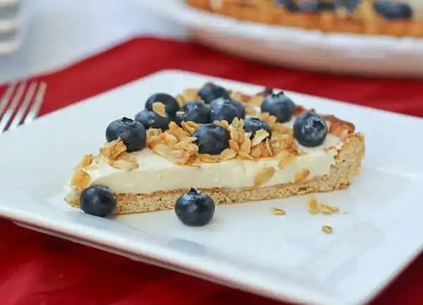 Front view of a slice of yogurt tart topped with blueberries and crunchy oat topping.
