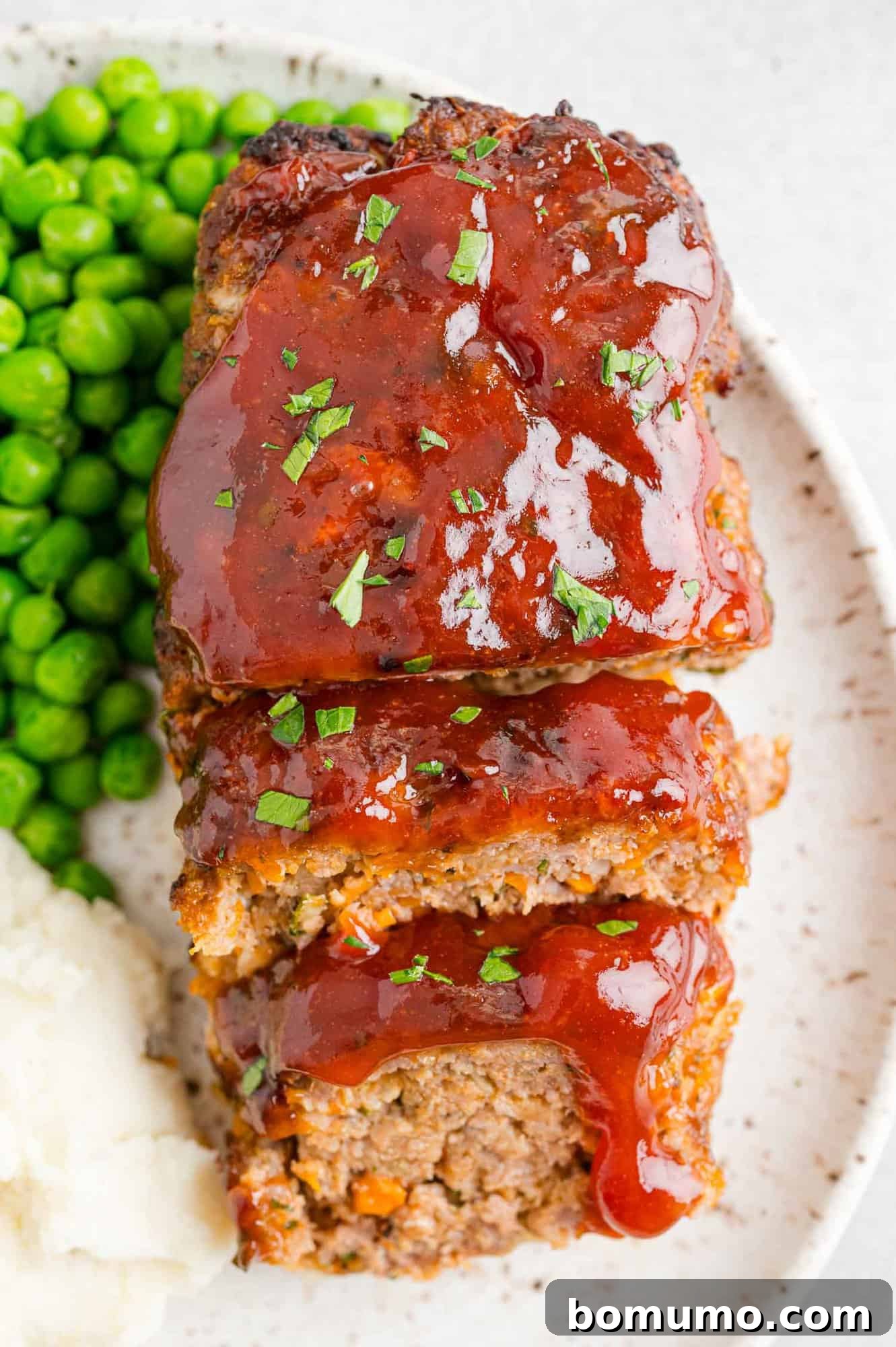 Perfectly sliced air fryer meatloaf, served on a plate alongside vibrant green peas and fluffy mashed potatoes, showcasing a golden-brown caramelized glaze.
