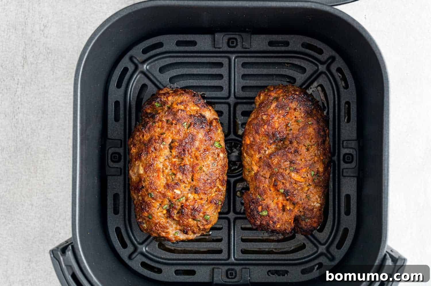 The two meatloaves cooking in the air fryer basket, showing a slight browning before the glaze is applied.