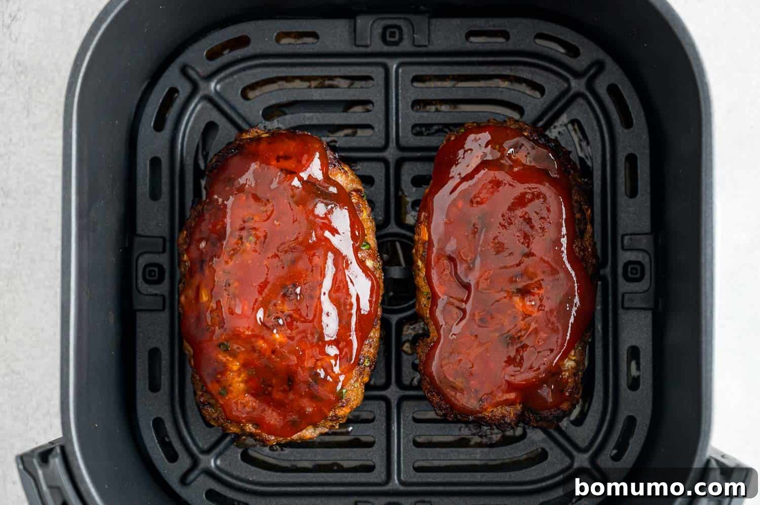 Air fryer meatloaf inside the air fryer, glistening with a newly applied, caramelized tomato-based glaze.