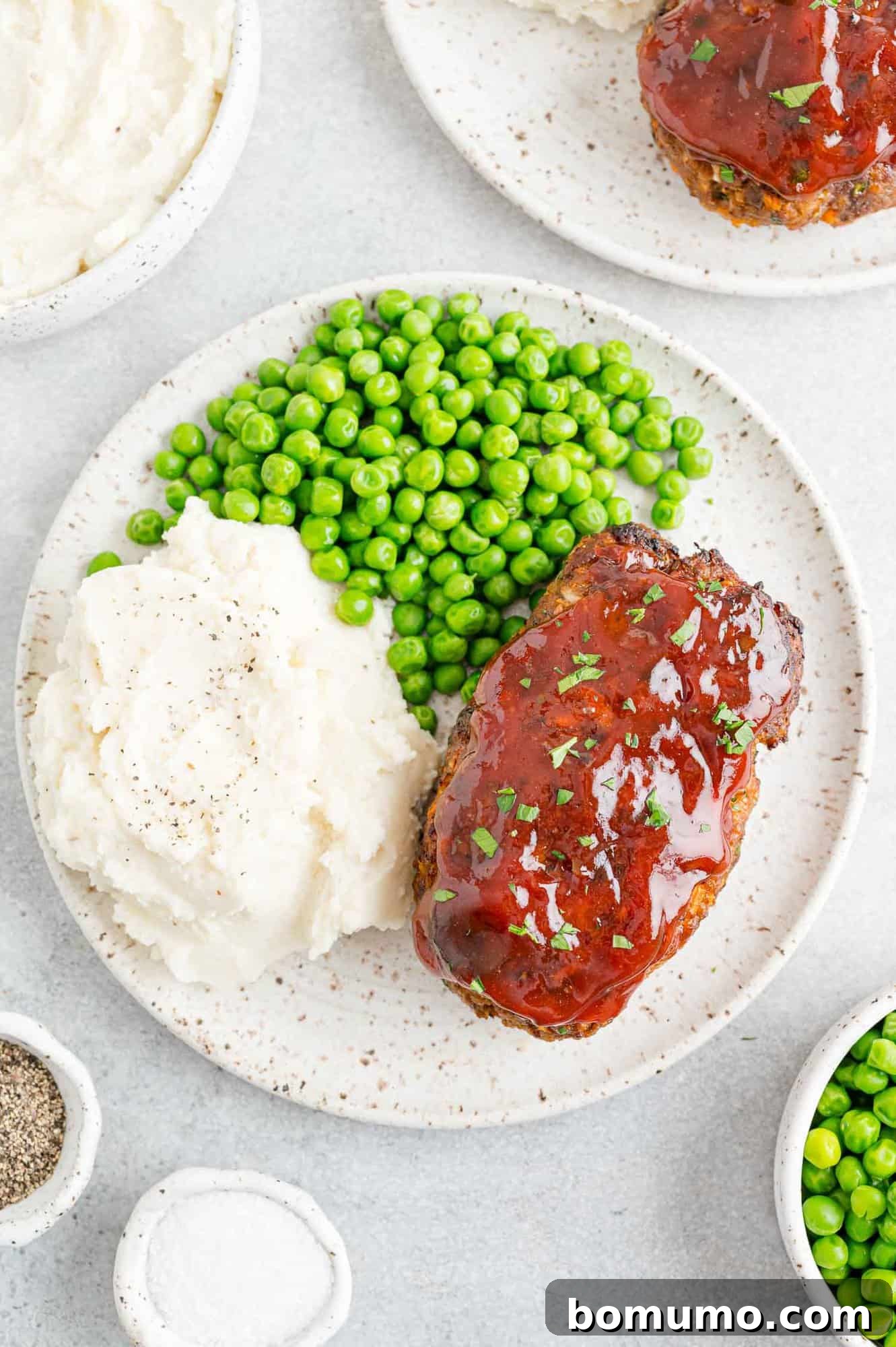 A close-up of air fryer meatloaf served with green peas and fluffy mashed potatoes, highlighting the rich, caramelized glaze.