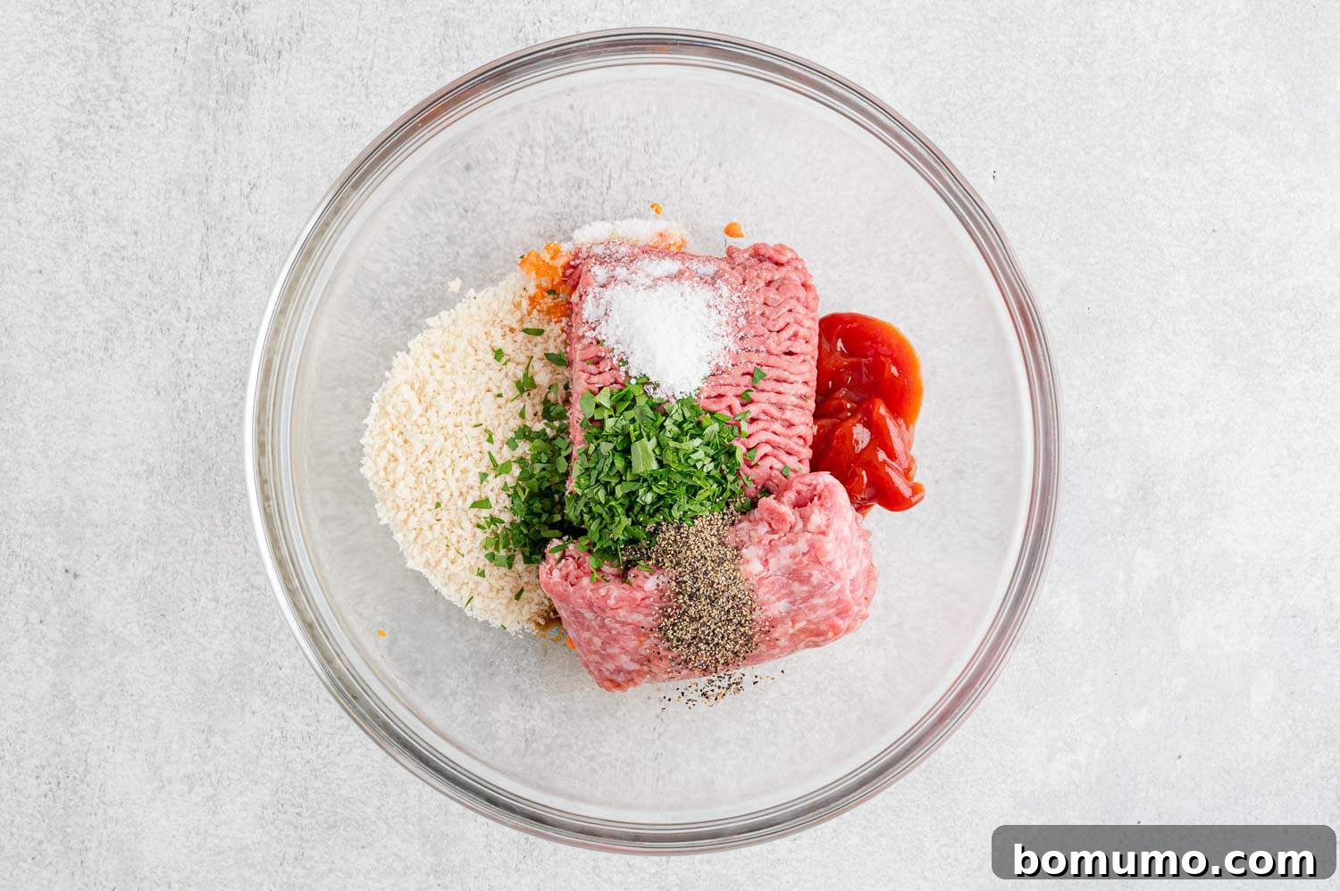 All meatloaf ingredients, including ground meats, vegetables, and seasonings, waiting to be mixed in a large bowl.
