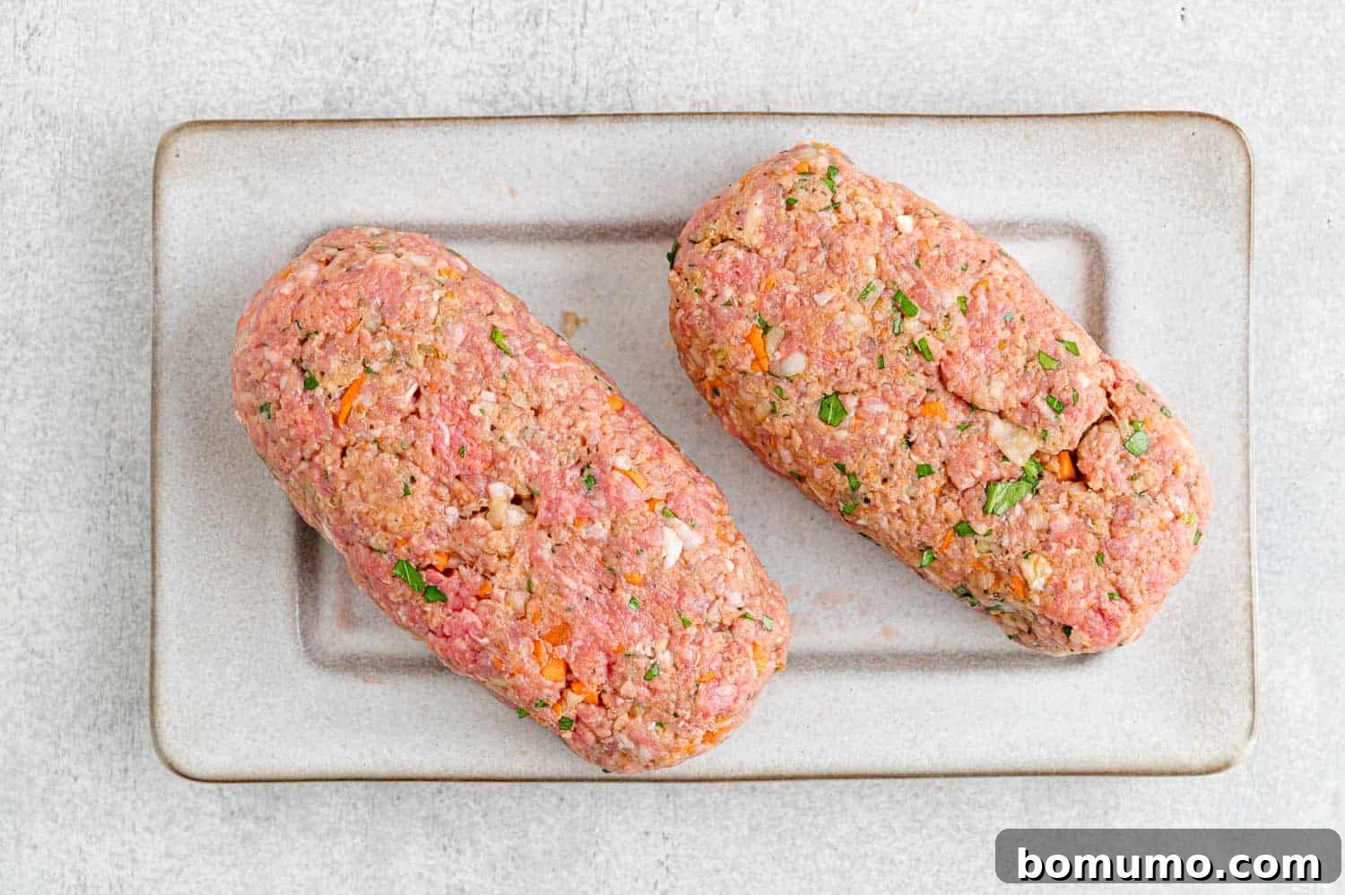 Two meatloaves meticulously shaped and ready for the air fryer, showcasing their uniform size and thickness.