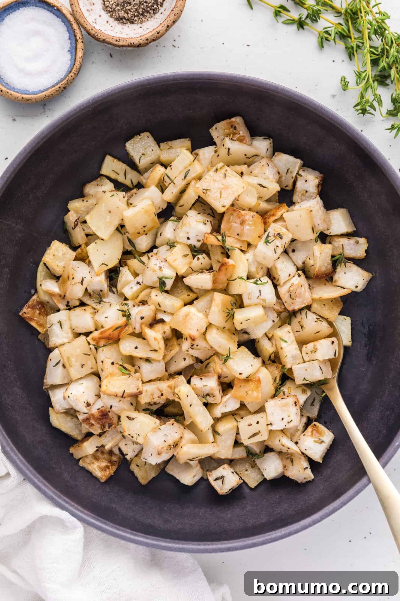 Roasted turnips in a large black serving bowl with spoon, garnished with fresh herbs.