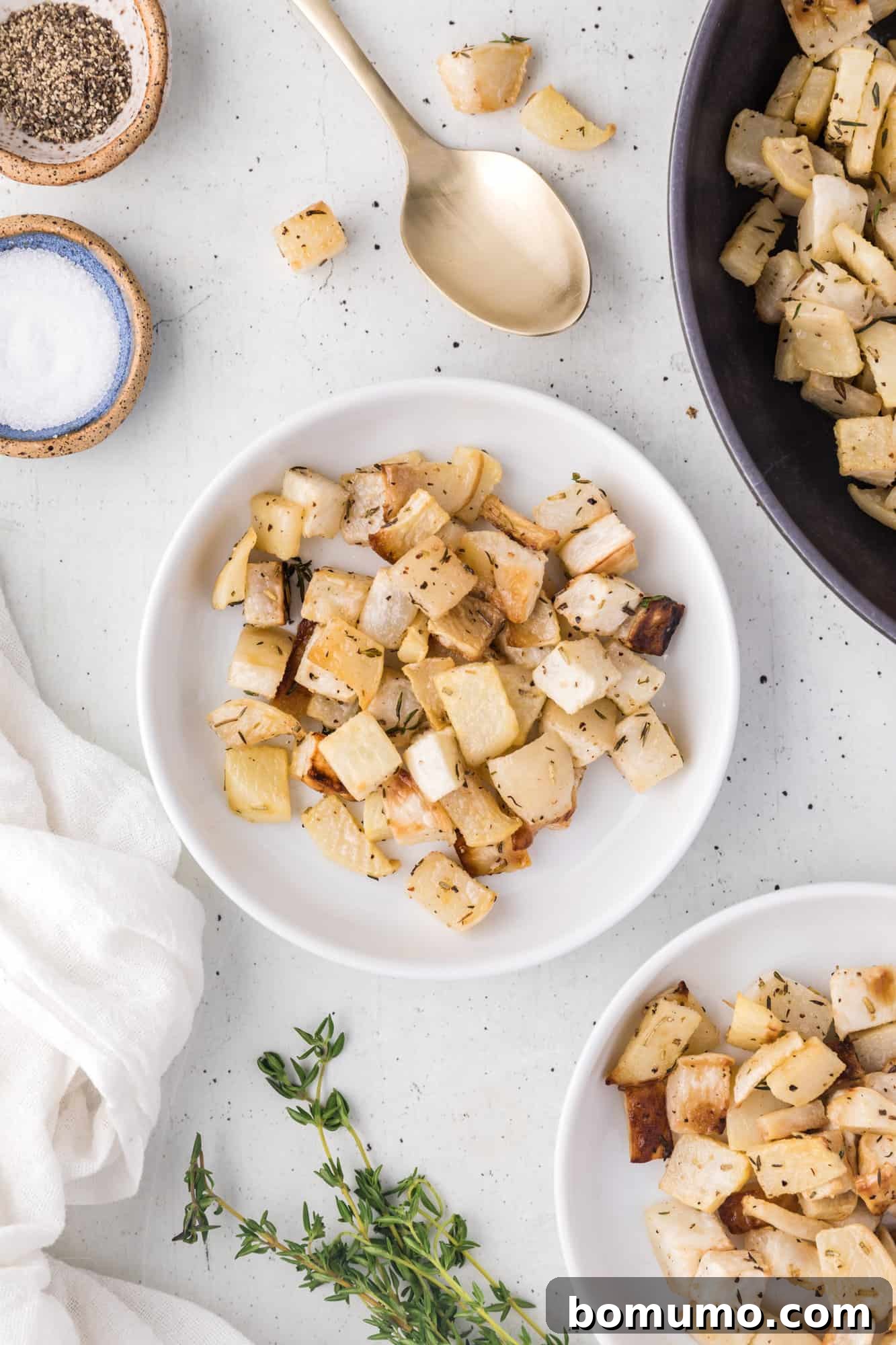 Roasted turnips on a white plate, surrounded by more turnips in a serving bowl, garnished with fresh herbs.