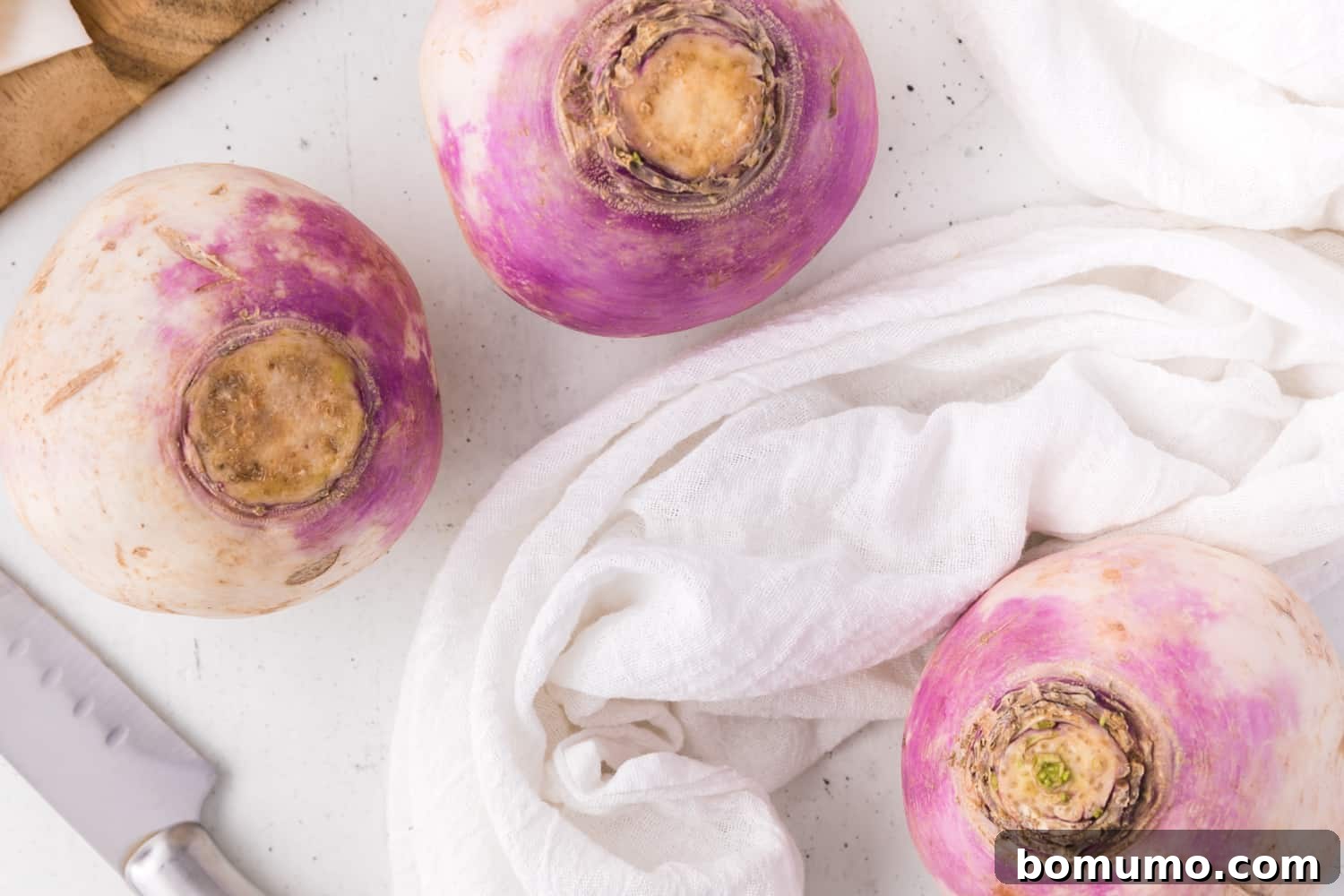 Three fresh turnips, with a white cloth, and a knife, ready for preparation.