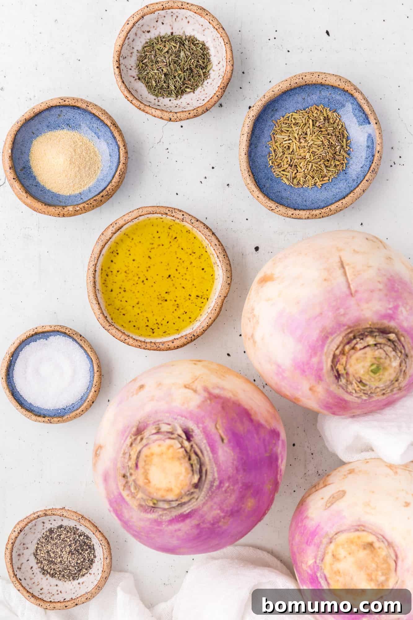 All essential ingredients for roasted turnips laid out on a countertop, including fresh turnips, olive oil, and herbs.