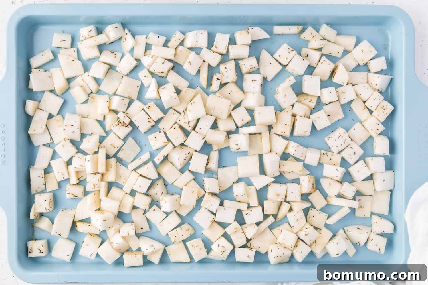 Uncooked, seasoned turnips spread evenly on a sheet pan.