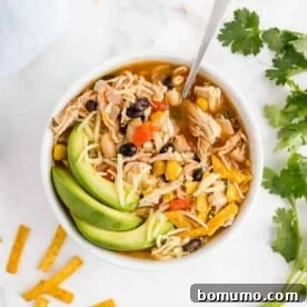 Chicken chili in a bowl garnished with avocado, cilantro, and cheese.