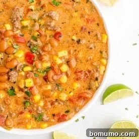 Overhead view of colorful creamy queso chili in a white bowl on a white surface, garnished with cilantro.