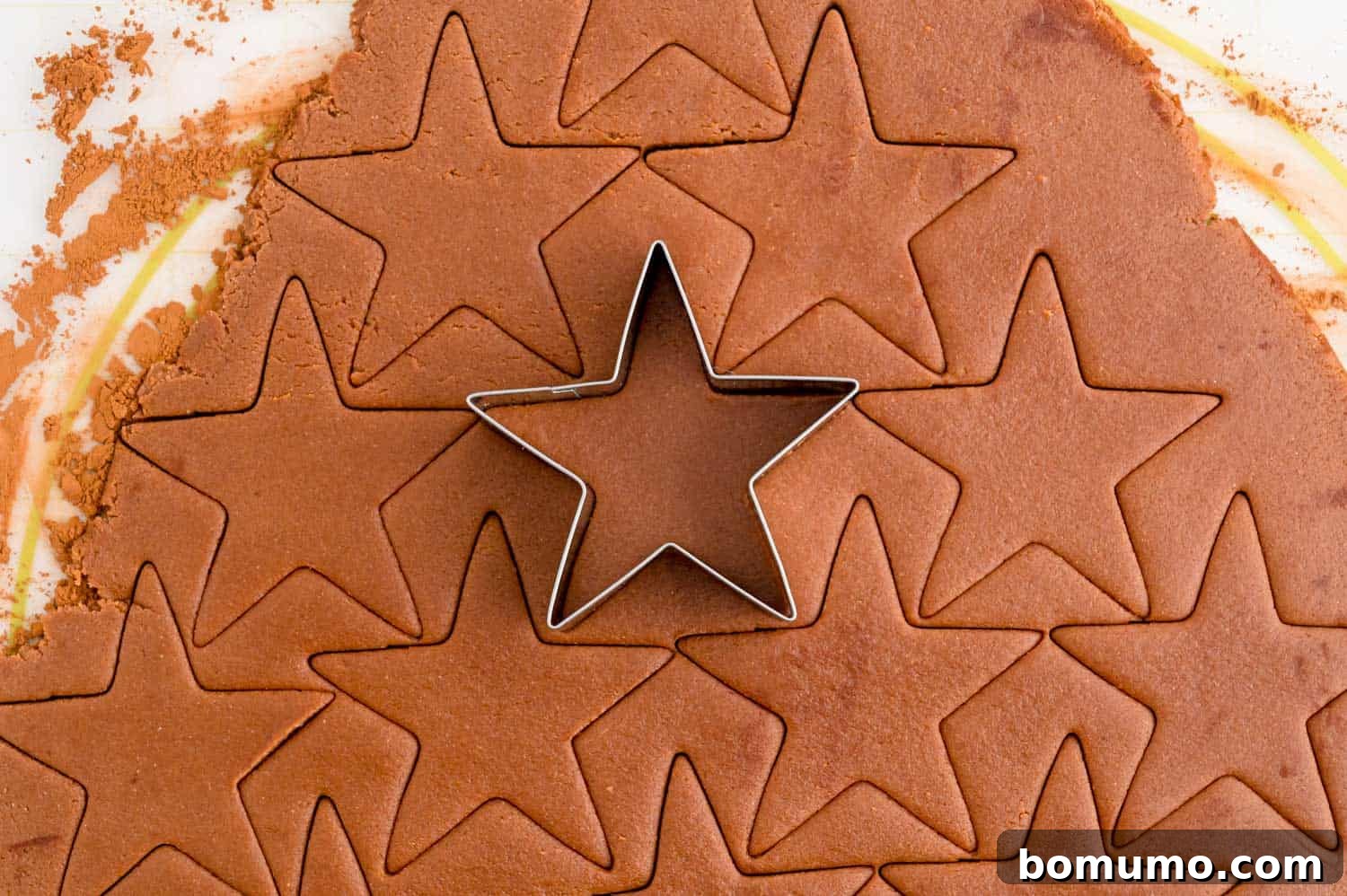 A festive star cookie cutter precisely shaping a peppermint chocolate sugar cookie from perfectly rolled-out dough on a cocoa-dusted surface.