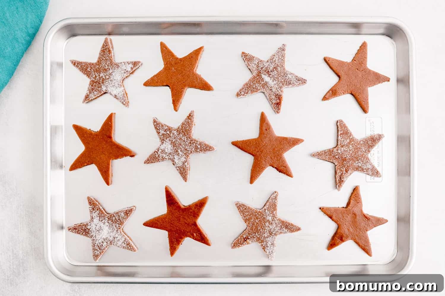 Multiple unbaked chocolate peppermint sugar cookies, perfectly cut into star shapes and neatly arranged on a parchment-lined cookie sheet, ready for baking in a preheated oven.
