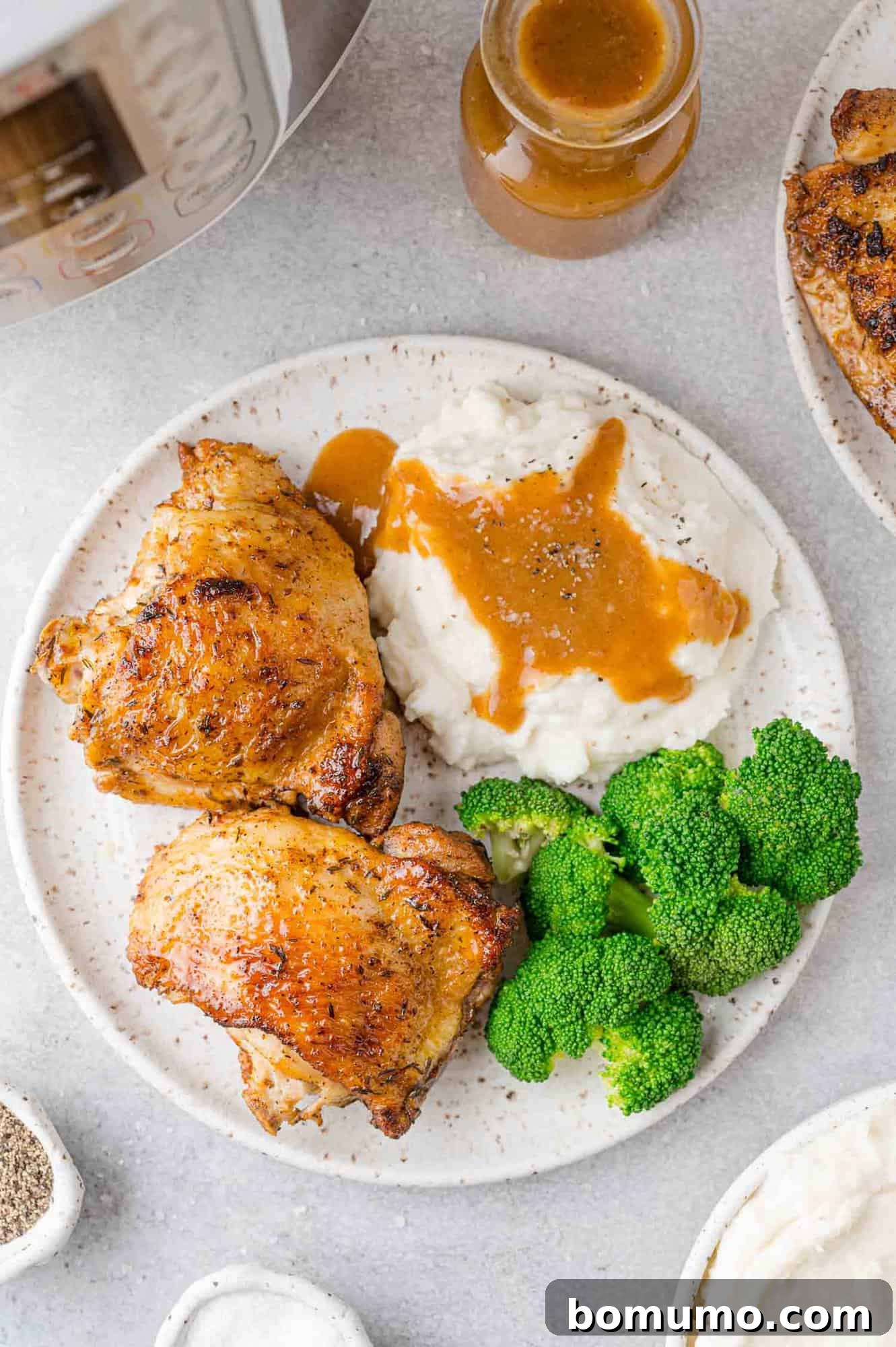 Overhead view of cooked chicken thighs on a plate with broccoli, mashed potatoes, gravy.