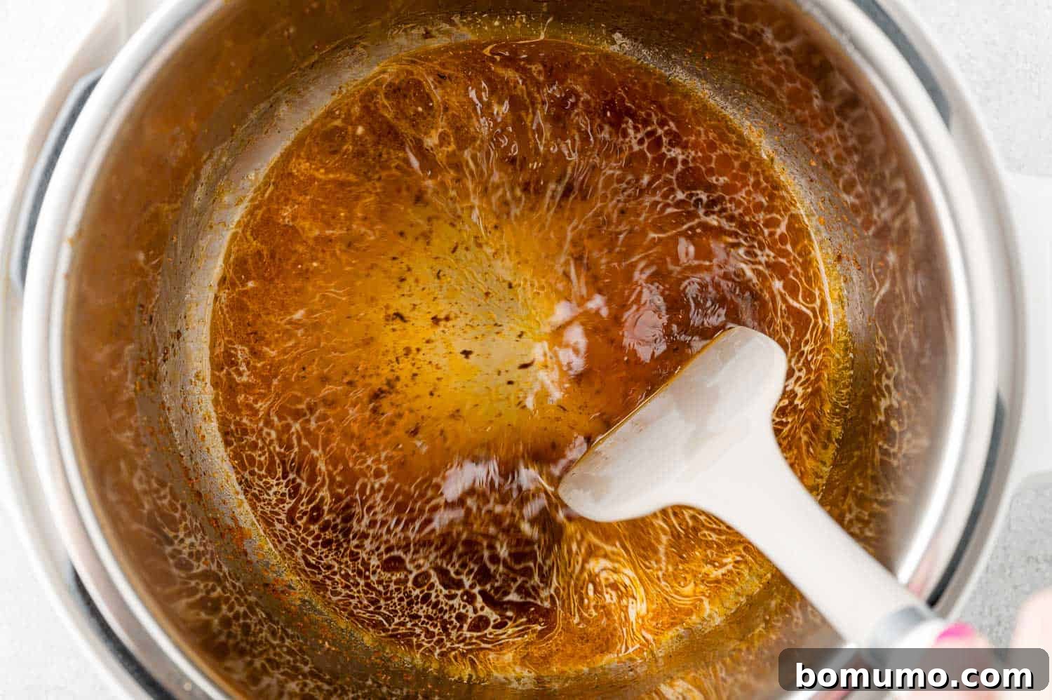 Chicken broth added to pot and brown bits being scraped off the bottom.