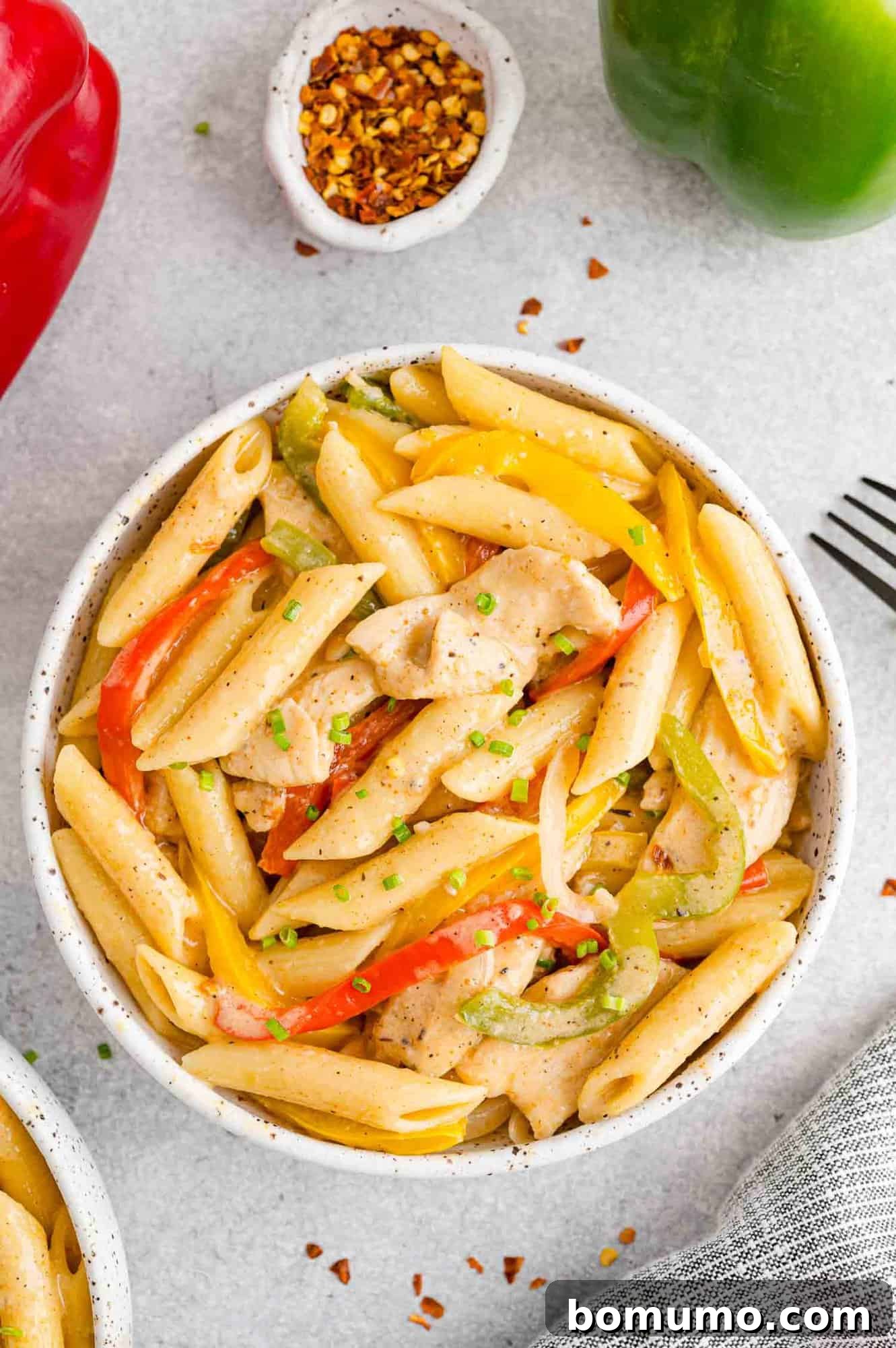 Overhead view of a bowl of Rasta Pasta next to a smaller bowl of crushed red peppers.