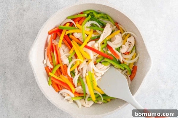 Sliced bell peppers and onions stirred in a skillet.