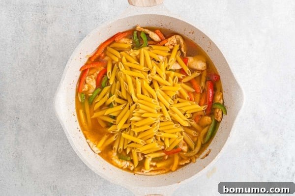 Ziti pasta added to a skillet with chicken and sauteed bell peppers.