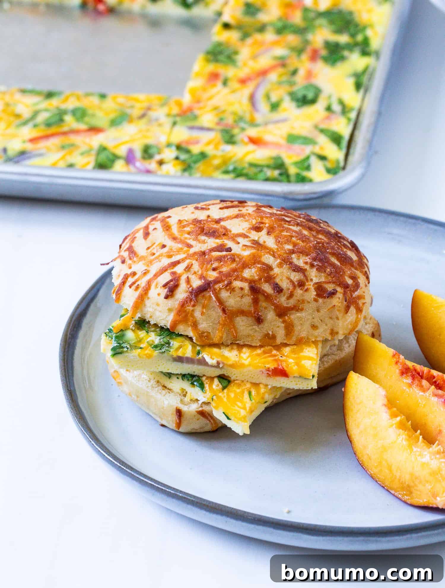A square of sheet pan scrambled egg, rich with add-ins, served on a delectable cheesy roll for a hearty breakfast.