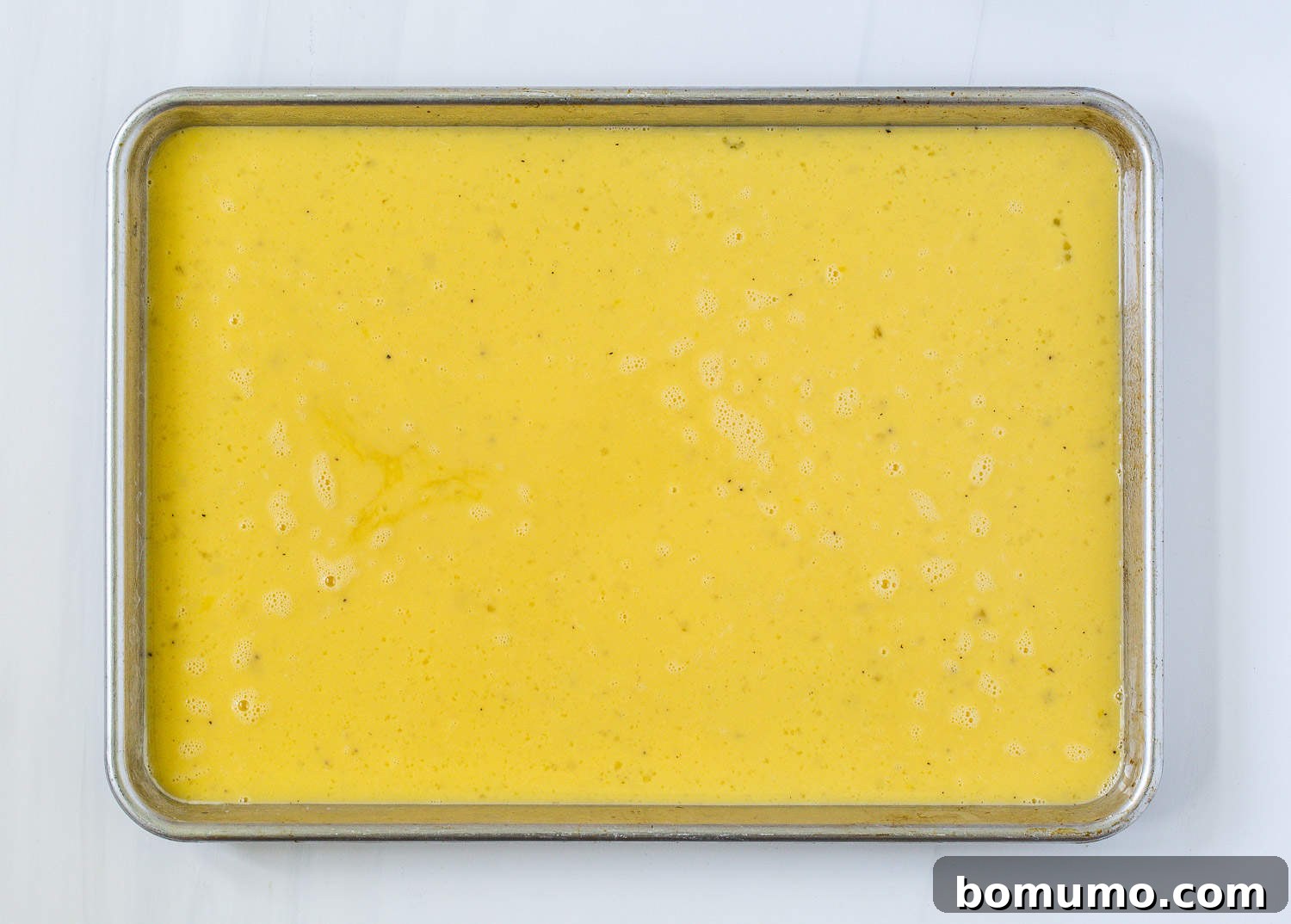 Liquid egg mixture poured evenly into a greased sheet pan, ready for toppings.