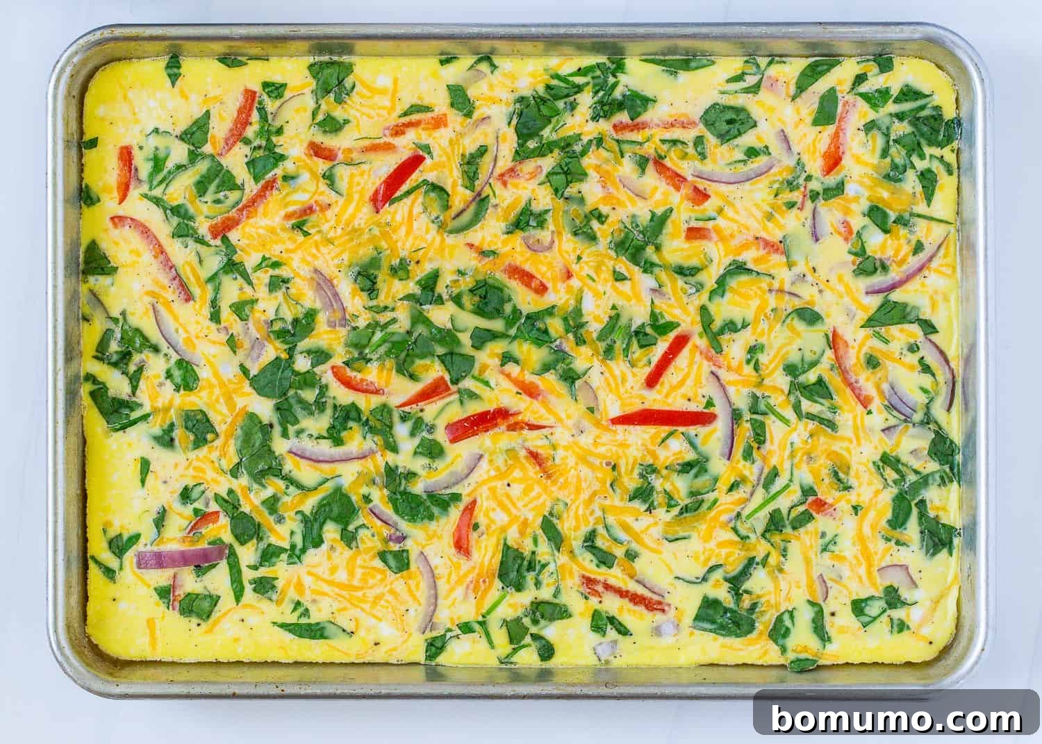Perfectly baked scrambled eggs, adorned with colorful vegetable add-ins, still in the sheet pan, ready to be sliced.