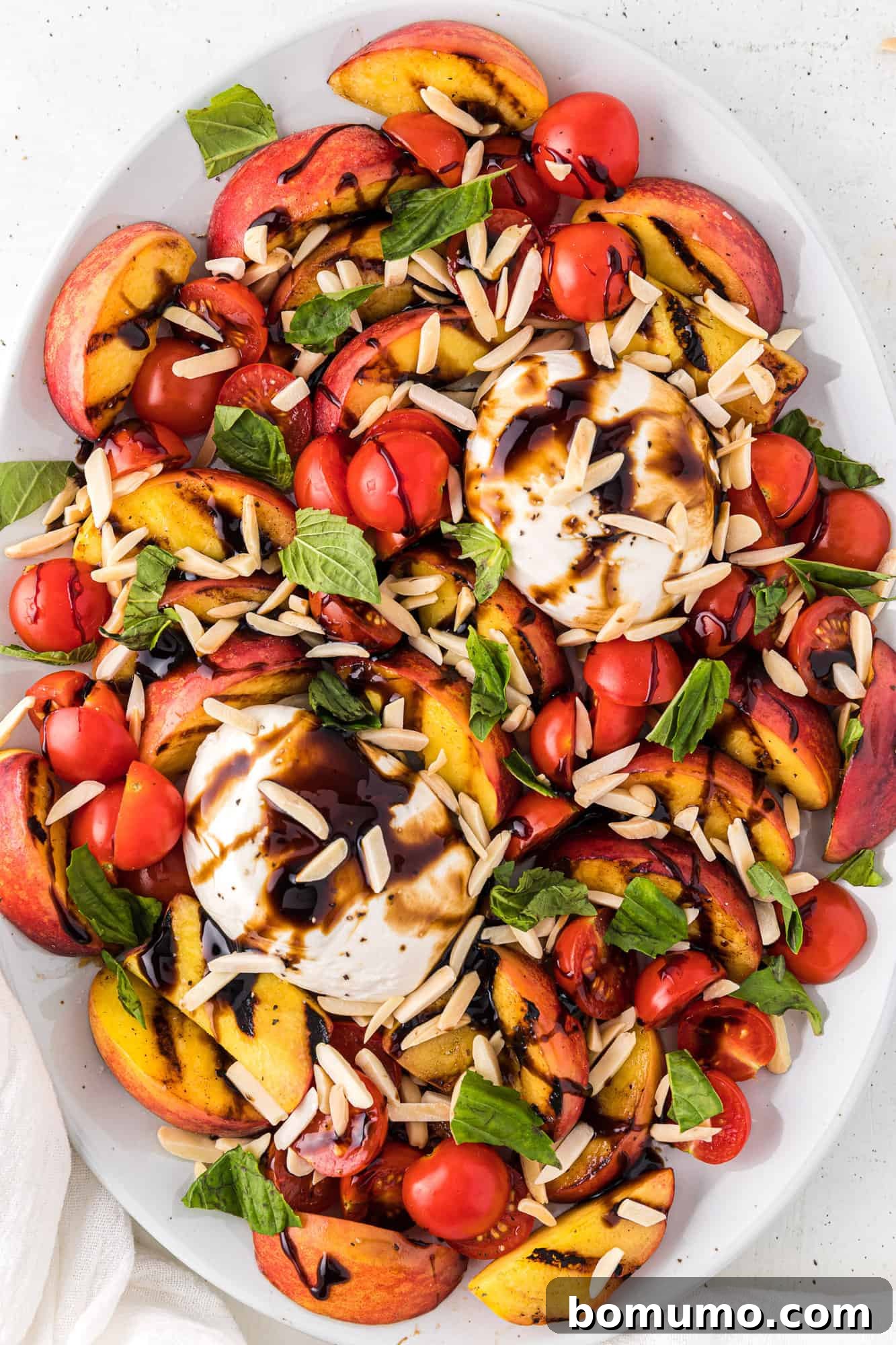 A vibrant grilled peach and burrata salad featuring golden grilled peaches, creamy burrata cheese, and fresh basil, artfully arranged and topped with toasted almonds.