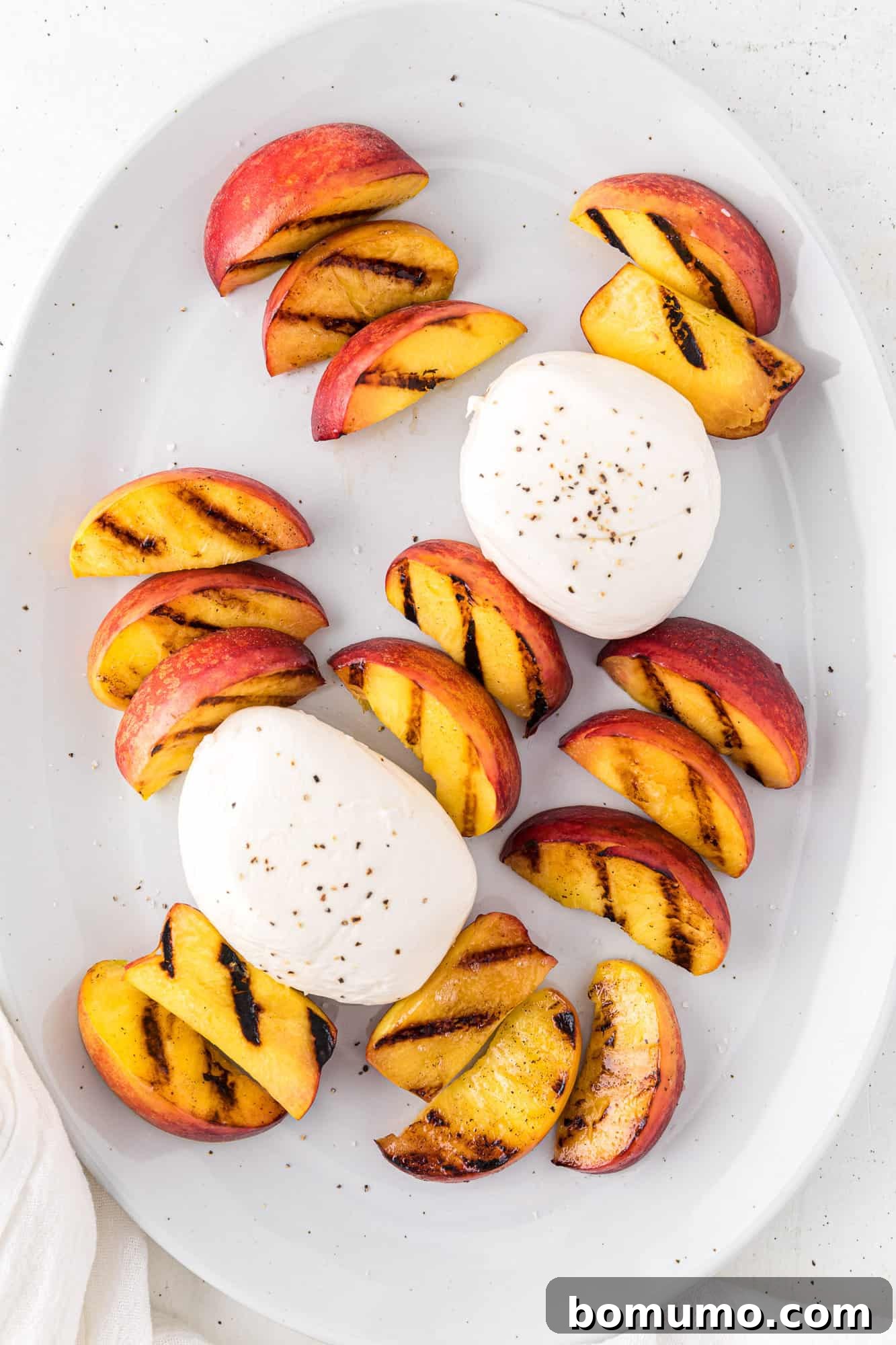 Grilled peach slices artfully arranged on a platter, encircling the creamy burrata cheese, forming the base of the salad.