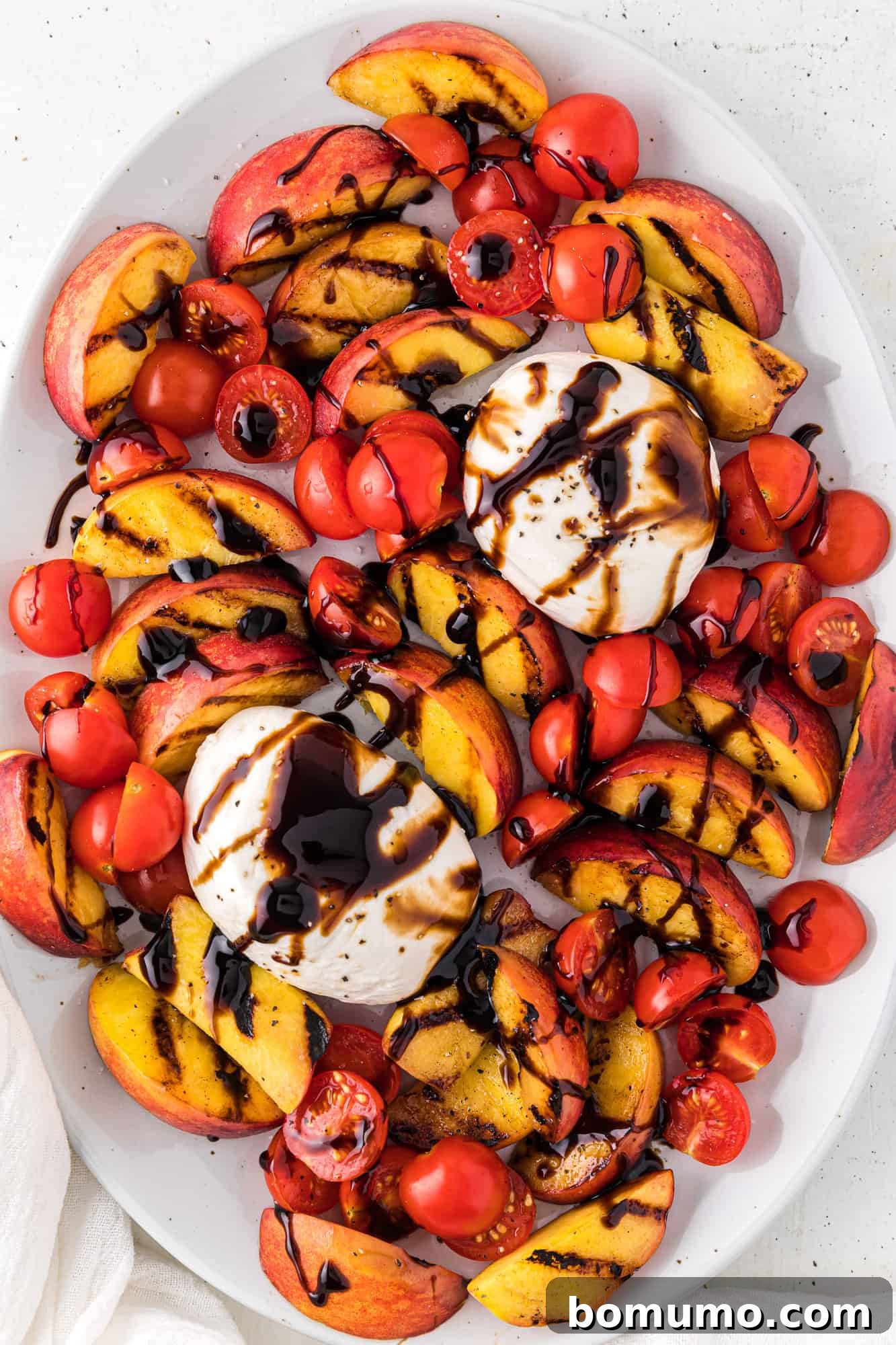 A generous drizzle of sweet and tangy balsamic glaze being applied over the grilled peach and burrata salad.