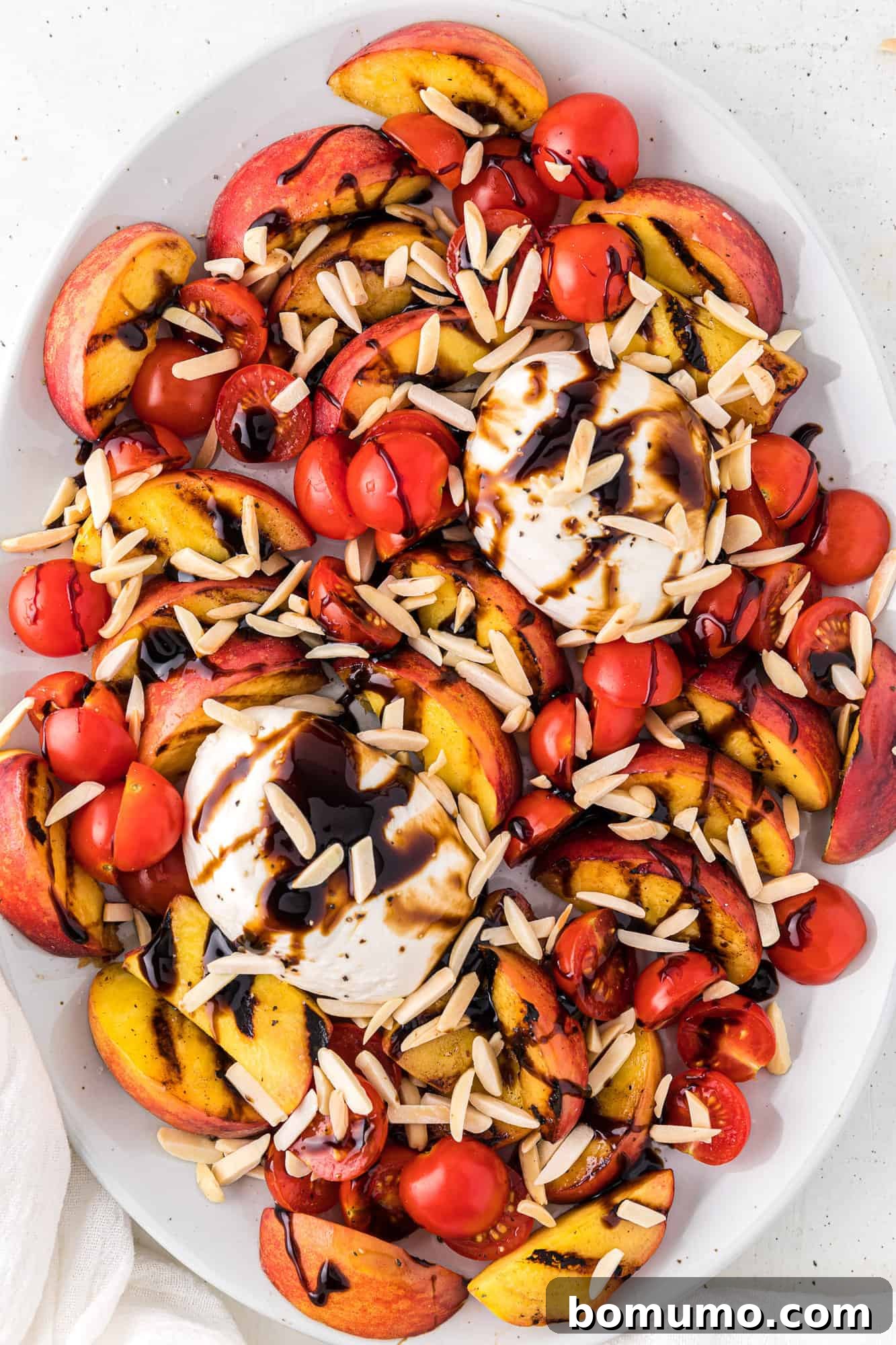 Crunchy toasted almonds being sprinkled evenly over the fresh grilled peach and burrata salad.