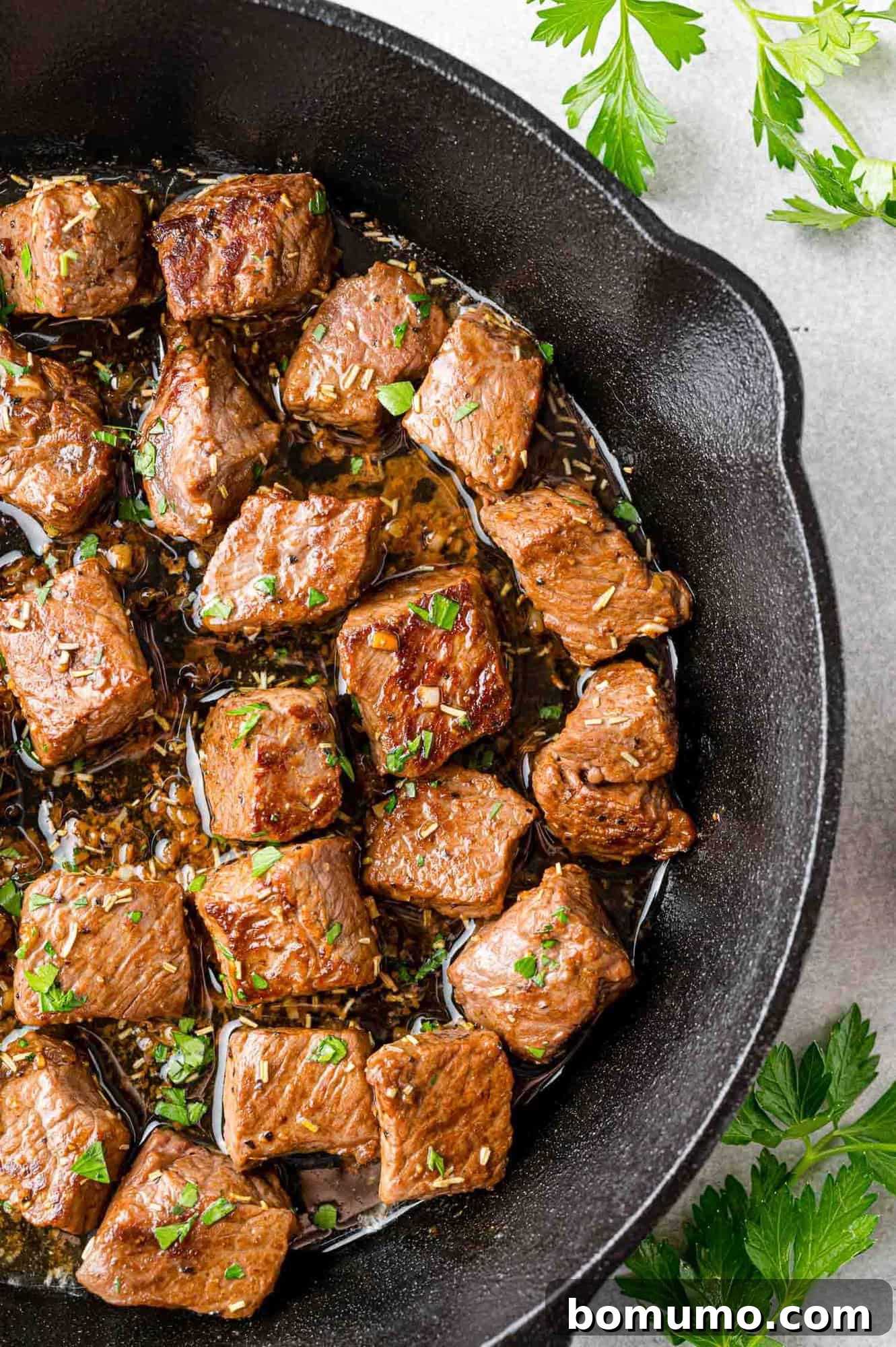 Sizzling steak bites coated in garlic butter, beautifully presented in a black skillet.