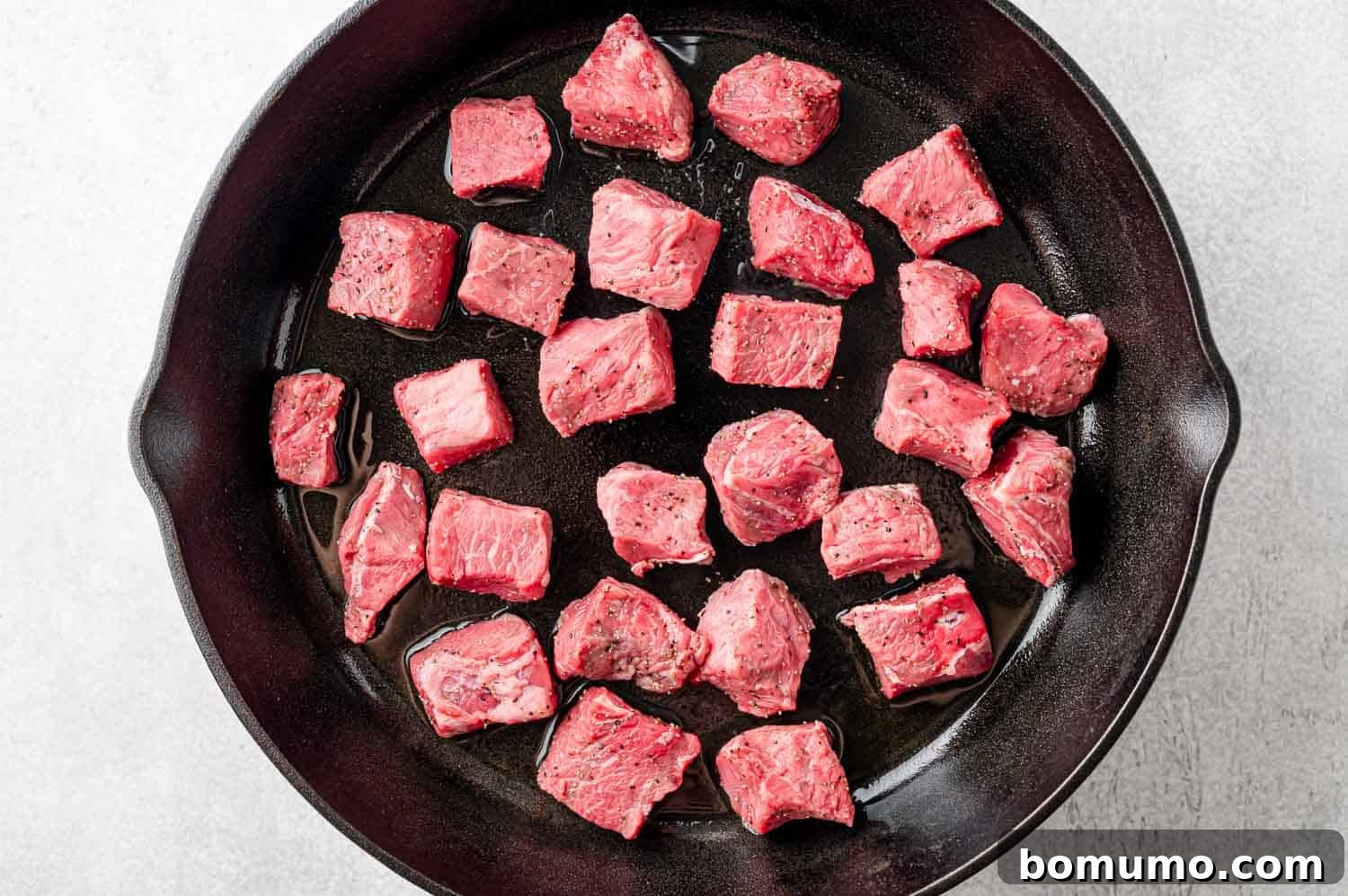 Uncooked steak bites arranged in a single, even layer within a hot skillet, ready for searing.