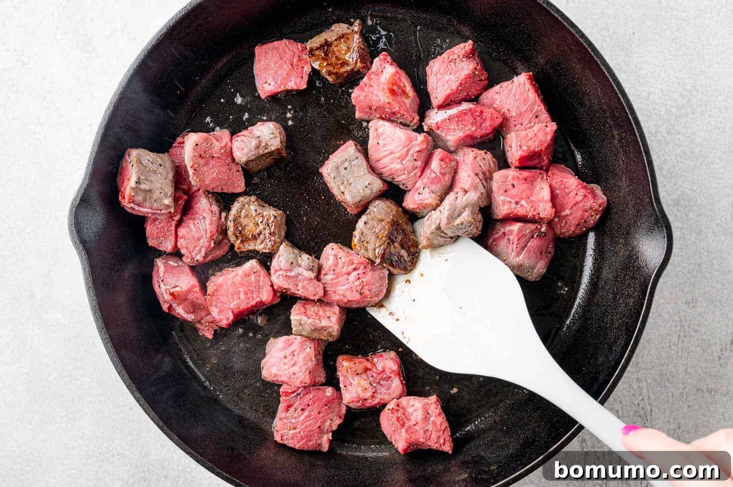 Steak bites midway through cooking, showing a beautiful sear, being stirred with a spatula.