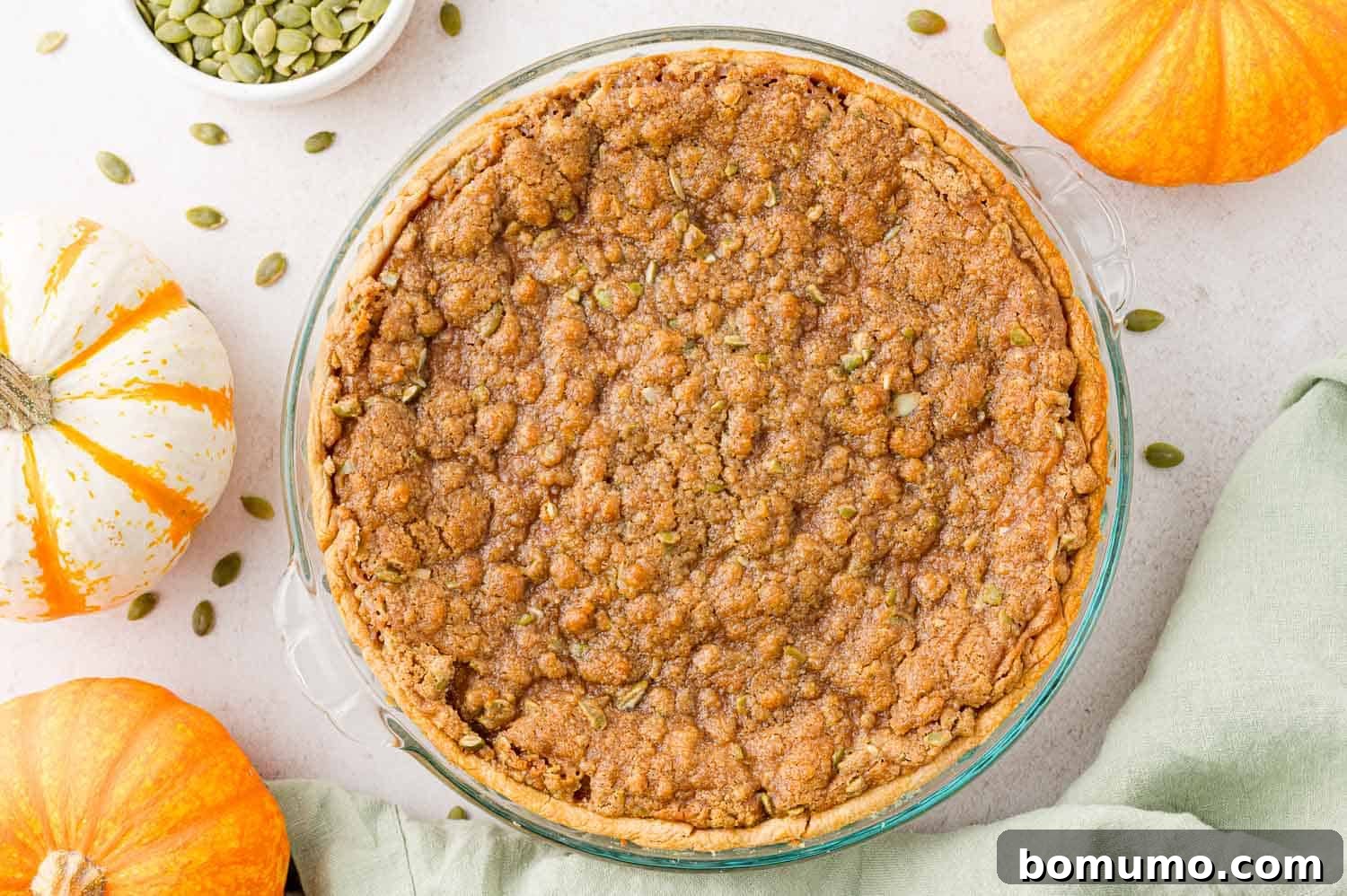 Baked pie, surrounded by small pumpkins and pepitas.