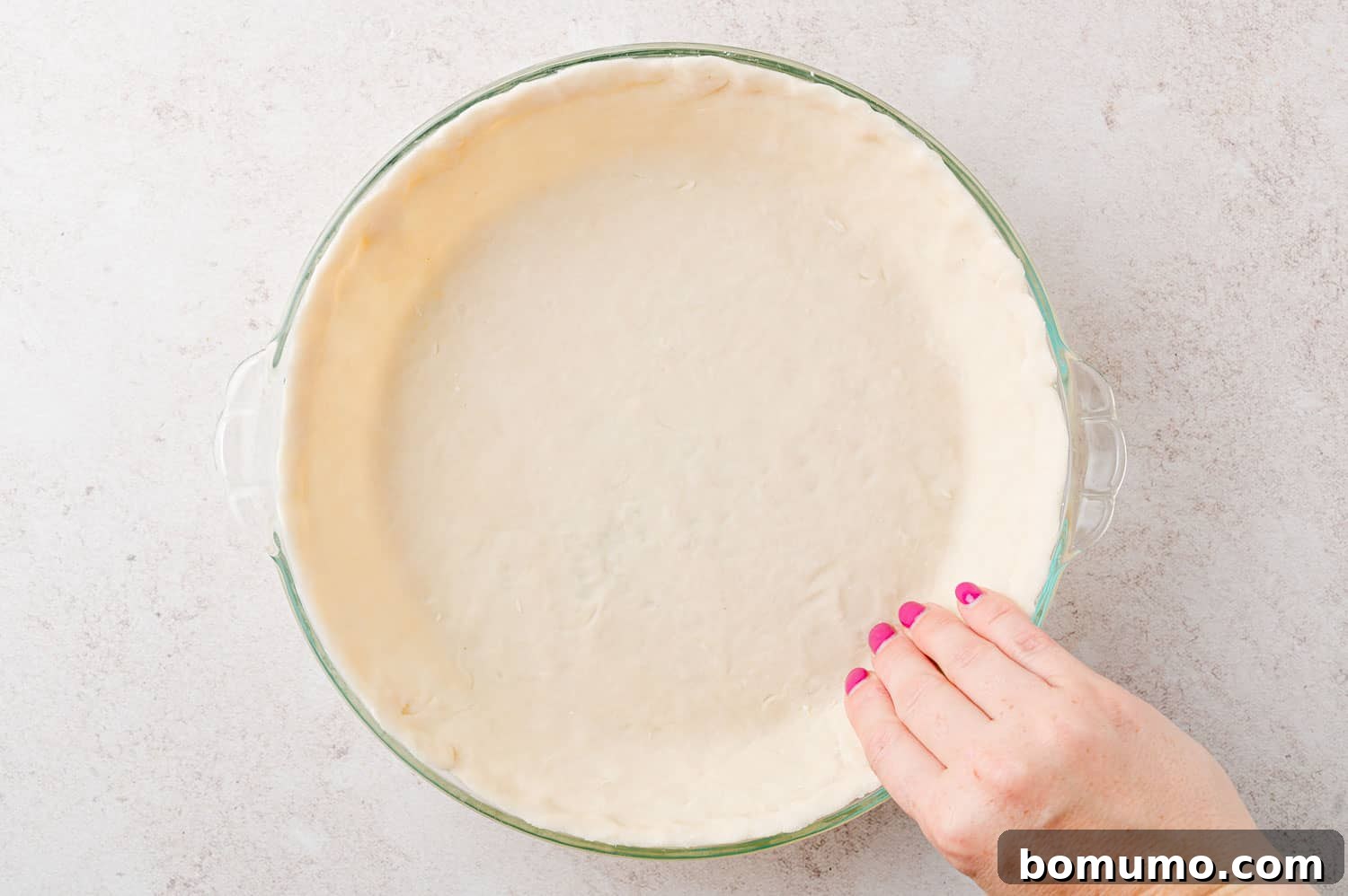 Crust being pressed into glass pie pan.