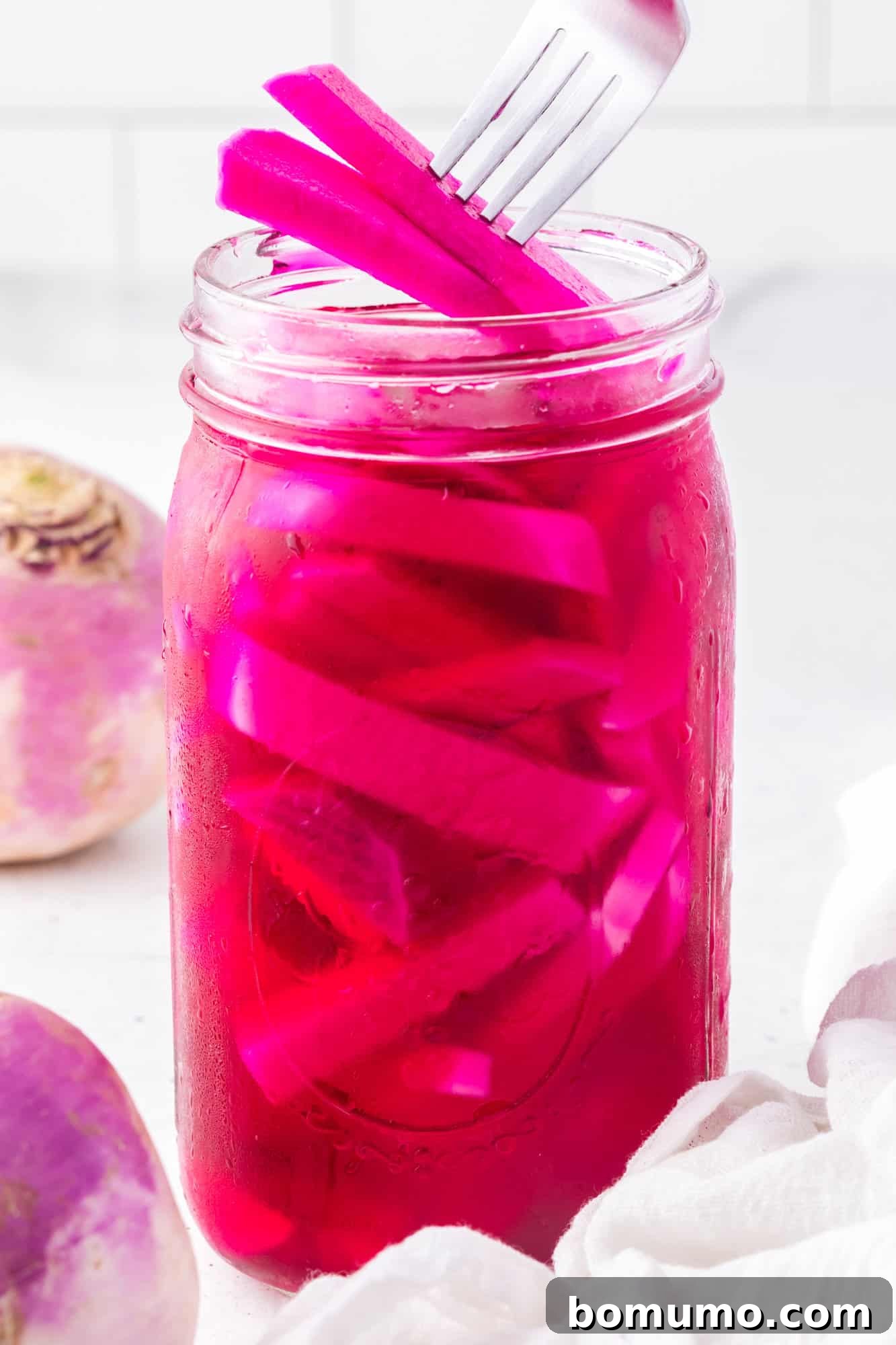 Pickled turnips being lifted out a jar with a fork.