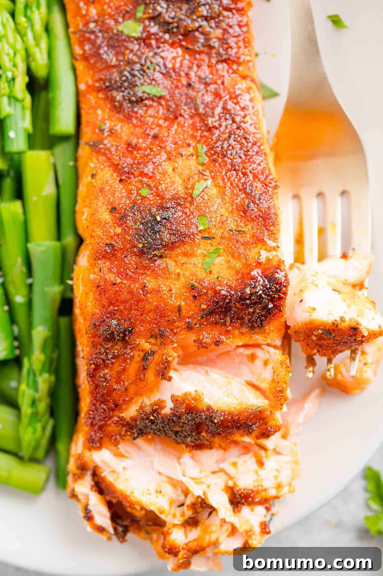 A forkful of salmon next to a flaked salmon filet on a plate with a side of green beans.
