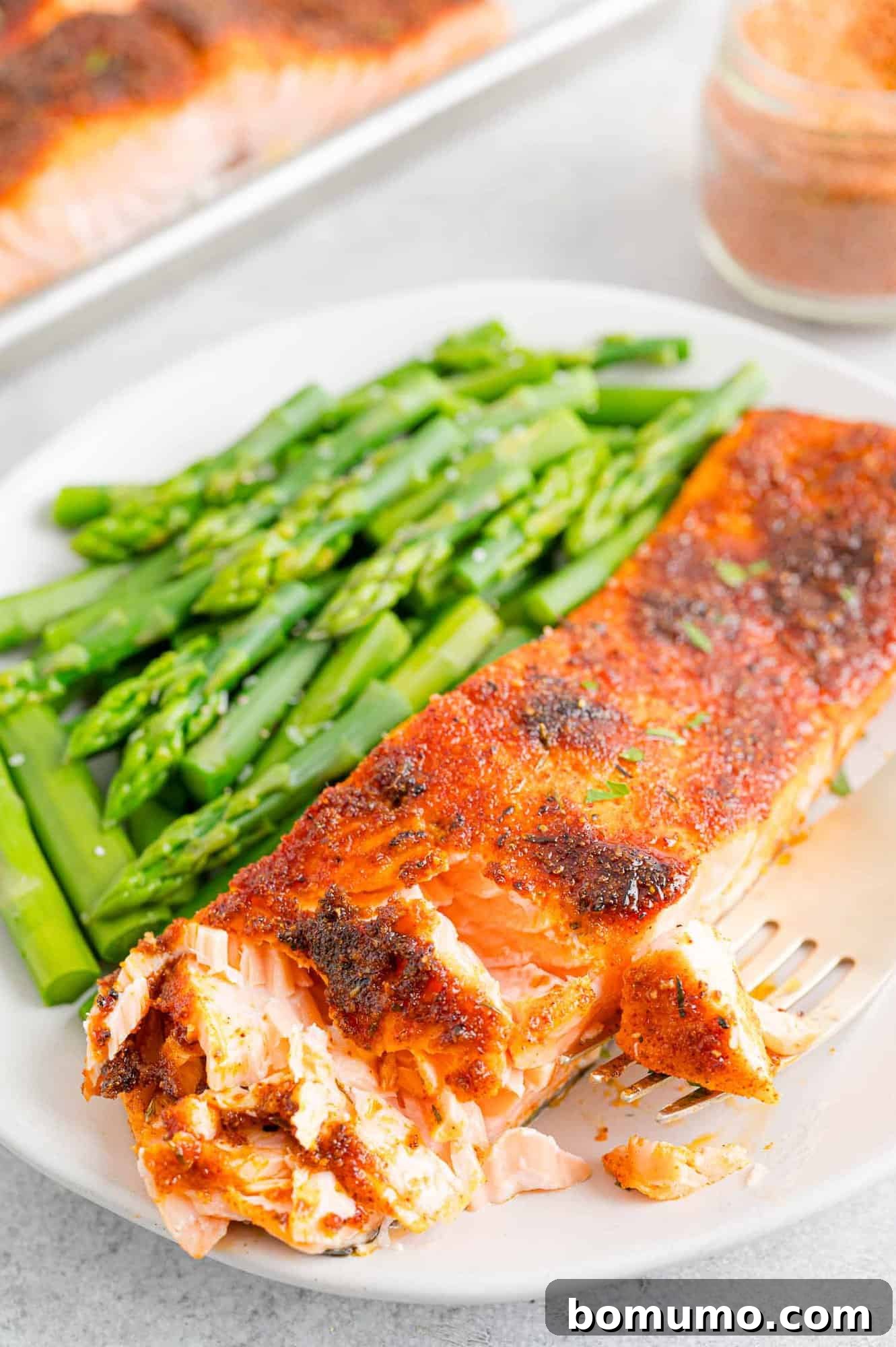A broiled salmon filet with the corner partially flaked, next to a side of green beans on a white plate.