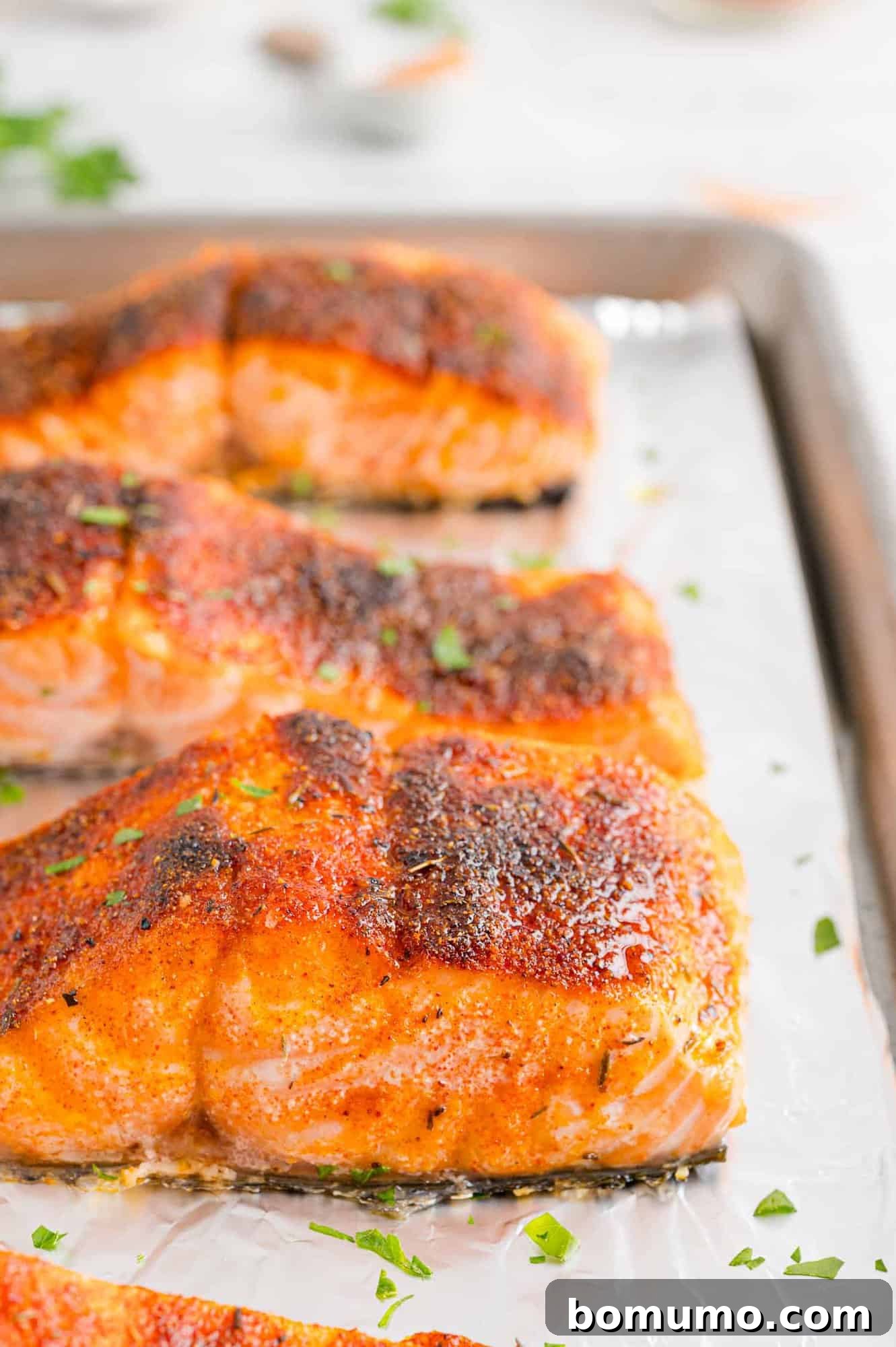 Close up side view of broiled salmon filets on a foil-lined baking sheet.