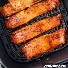 Four glazed salmon fillets in an air fryer basket, cooked to a perfect golden brown, ready to serve.