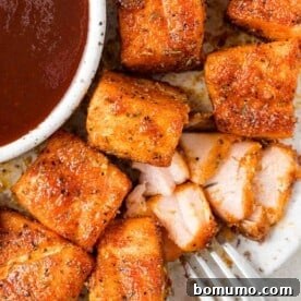 Air fryer salmon bites on a plate, one flaked open to show its tender, juicy texture.