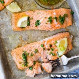 Easy baked salmon with fresh lemon slices and delicate chives, served on a sheet pan.