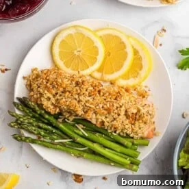 Overhead view of almond and parmesan crusted salmon on a plate, elegantly served with lemon slices and crisp asparagus.