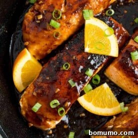 Vibrant orange glazed salmon in a frying pan, showcasing a glossy, appetizing finish.